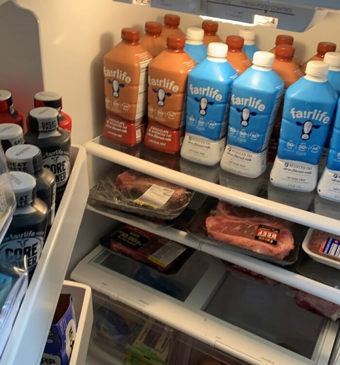 Inside view of a refrigerator filled with milk cartons and raw meat, showcasing a chaotic dude fridge.