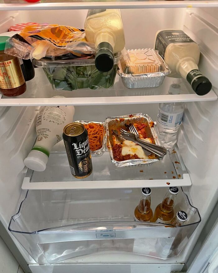 Chaotic dude fridge with leftover food, beer, and condiments scattered on shelves.