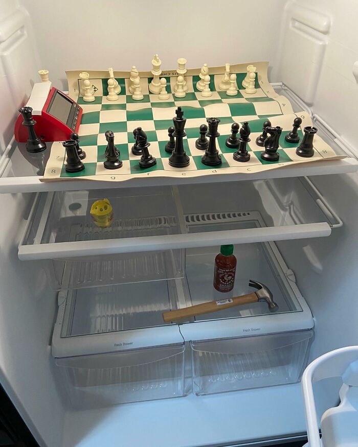 Chessboard in a fridge with Sriracha, hammer, and egg timer, showcasing 'Dude Fridges' chaos.