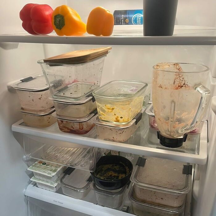 Chaotic dude fridge with random containers, a blender, bell peppers, and drink can on shelves.