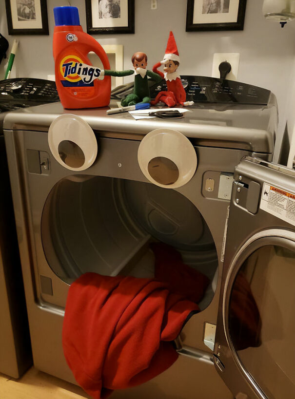 "Elf On The Shelf idea with elves sitting on top of a dryer decorated with googly eyes and a red blanket resembling a tongue, making it look like a face."