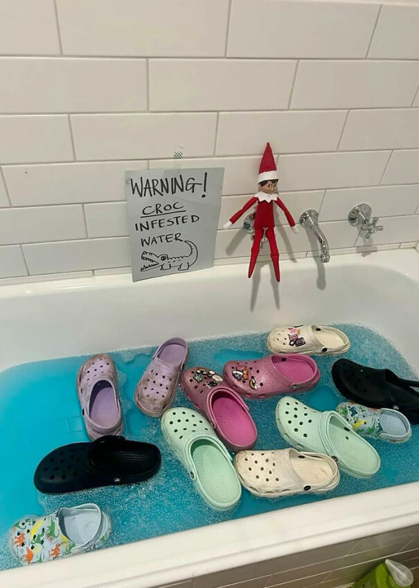 "Elf On The Shelf idea with an elf hanging above a bathtub filled with 'Croc-infested' water, featuring various Crocs shoes floating on blue water."