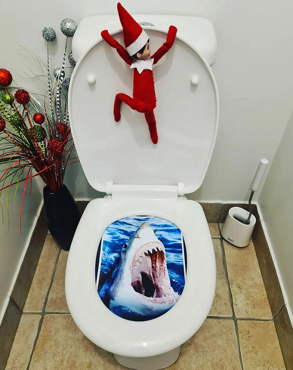  "Elf On The Shelf idea with an elf clinging to a toilet seat, which has an image of a shark’s open mouth, creating a humorous 'shark attack' scene."