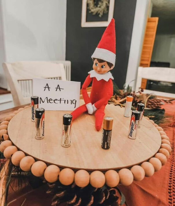 "Elf On The Shelf idea with the elf attending an 'AA meeting' surrounded by AA batteries, playfully referencing Alcoholics Anonymous."