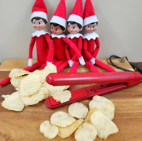 "Elf On The Shelf idea with four elves seated behind a hair straightener, appearing to make homemade potato chips on a wooden surface."