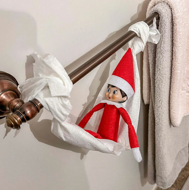 "Elf On The Shelf idea with an elf sitting in a hammock made from a roll of toilet paper hanging on a towel bar in the bathroom."