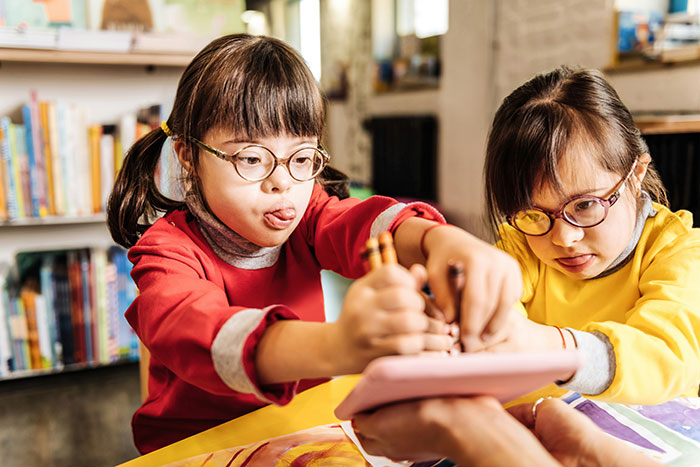 Two young girls with glasses drawing together at a table, expressing creativity and focus.