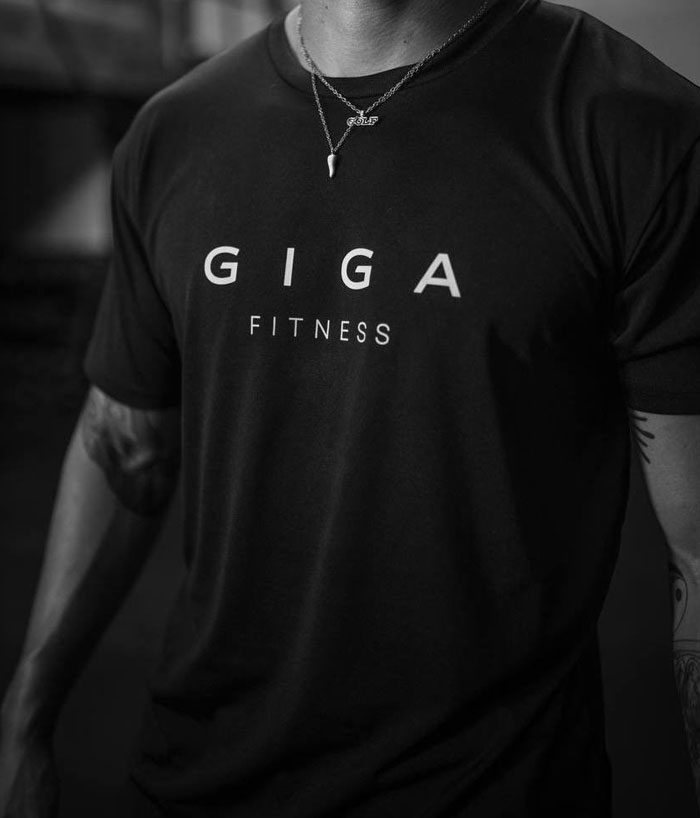 A grayscale image showing a person wearing a T-shirt with "GIGA FITNESS" printed on it, referencing the Giga Chad meme branding.