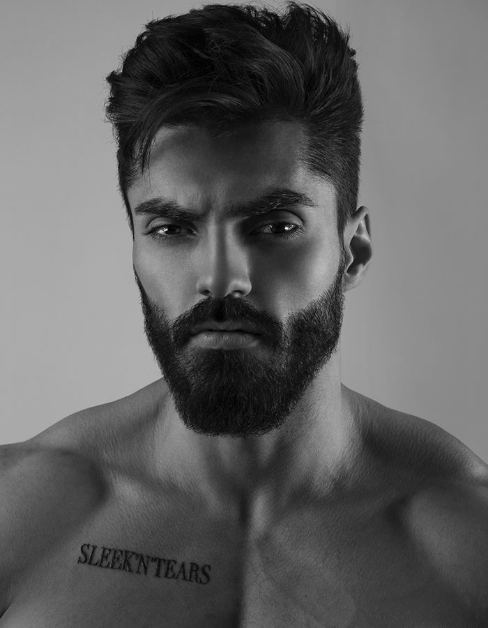 A grayscale portrait of a muscular man with sharp features, a beard, and "SLEEK'N'TEARS" tattooed on his chest, tied to the Giga Chad meme.