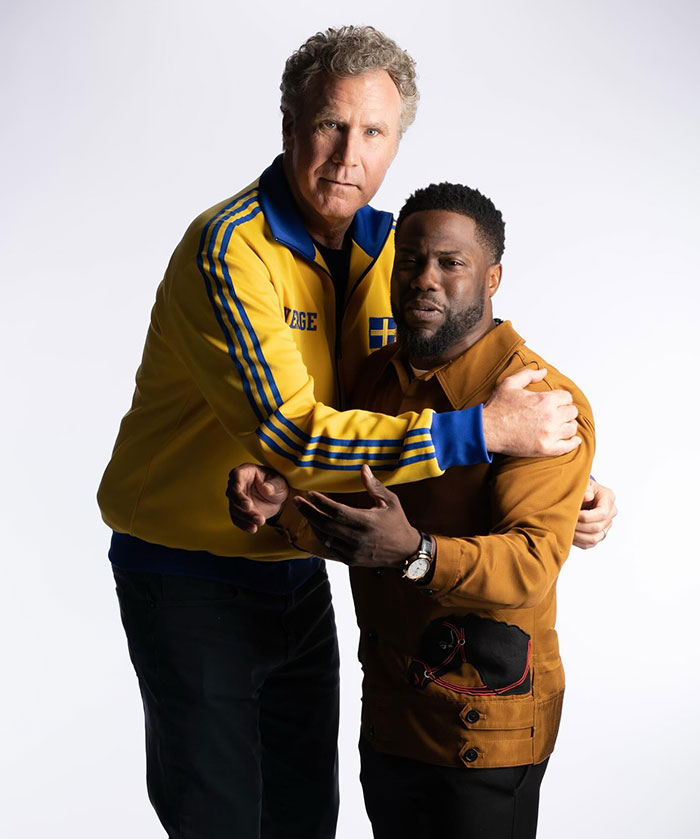 A tall man in a yellow Swedish jacket hugs Kevin Hart, who is wearing a brown shirt, emphasizing their notable height difference.