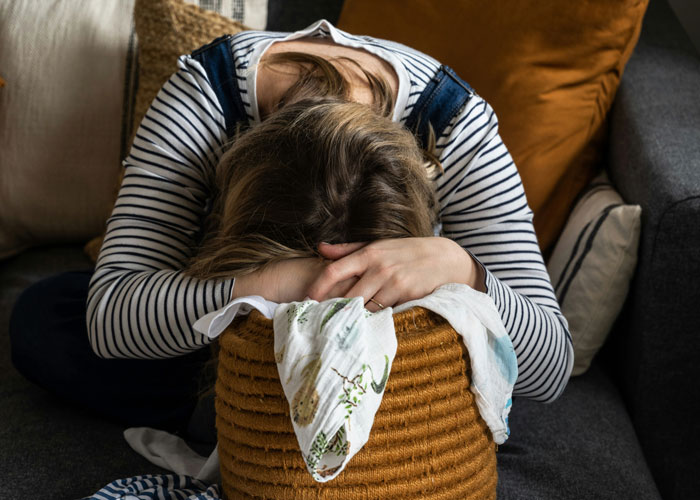 Woman resting head on wicker basket, appearing frustrated.