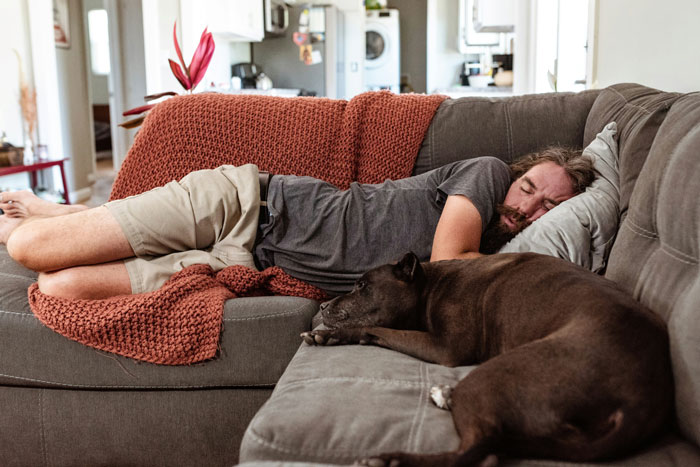 Man sleeping on the couch with a dog, illustrating a husband in an intimate home setting.