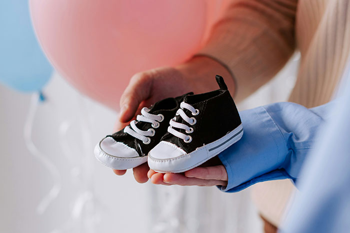 Hands holding baby shoes, symbolizing the experience of having a baby at a young age.