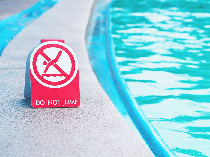 Safety sign by a pool edge with "Do Not Jump," highlighting safety concerns.