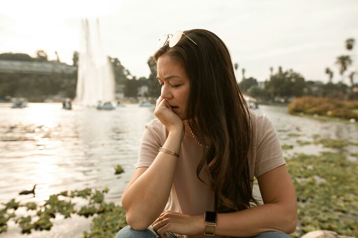 Grieving mother-in-law sitting by a lake, looking contemplative and concerned.