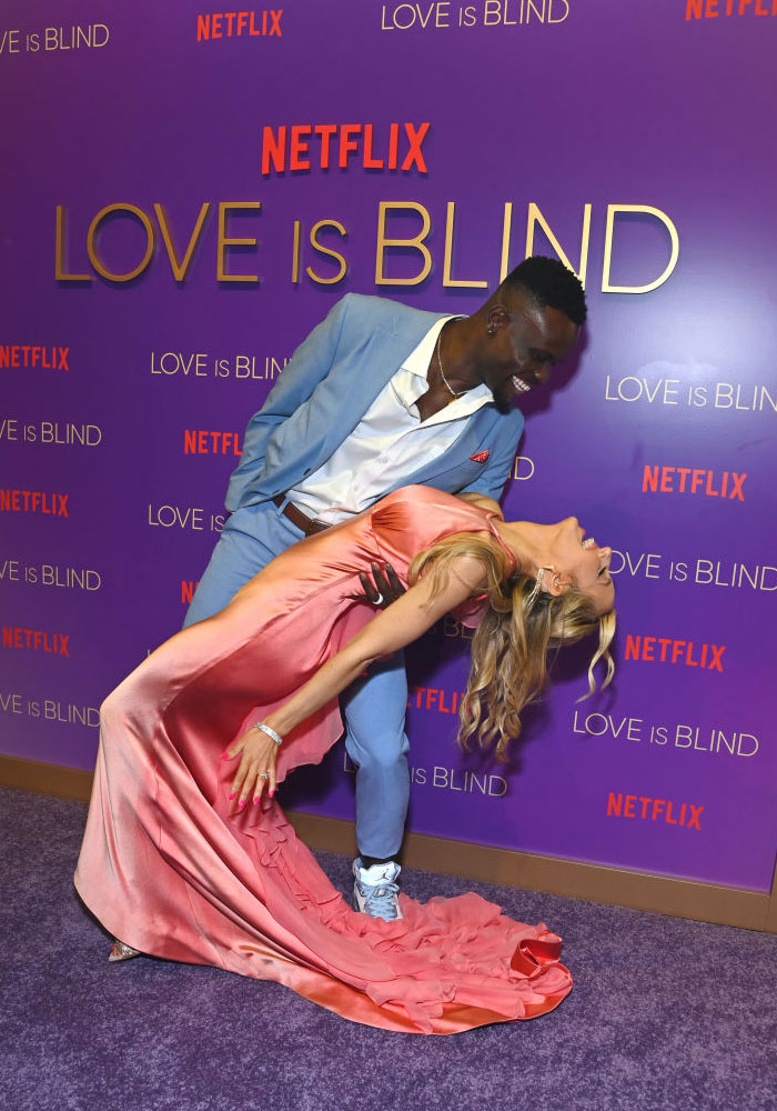 Couple posing at a "Love Is Blind" event, with the woman in a pink dress and the man in a blue suit.