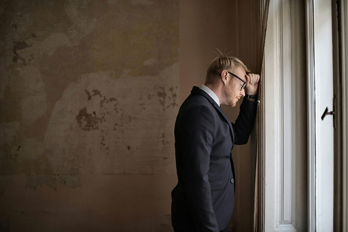 A man in a suit looking shocked, standing by a window, pondering an unexpected event related to wife and twins.