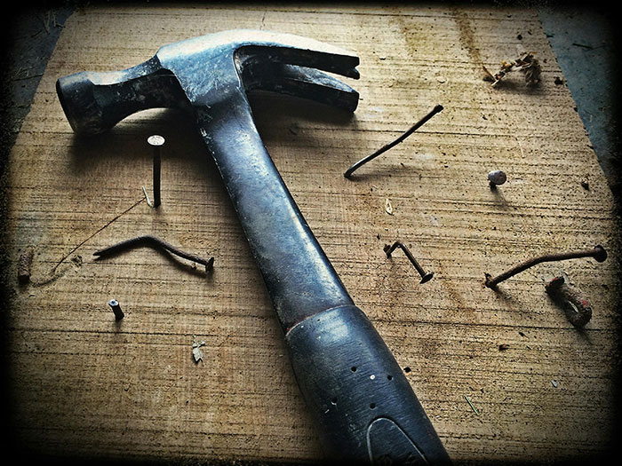 Hammer and scattered nails on wooden surface, reflecting urgency and unexpected chaos.