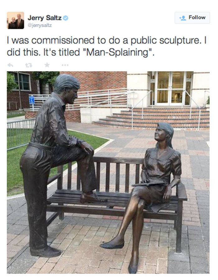 A mansplaining meme featuring a tweet by Jerry Saltz showing a sculpture titled "Man-Splaining," with a man leaning toward a seated woman on a bench.