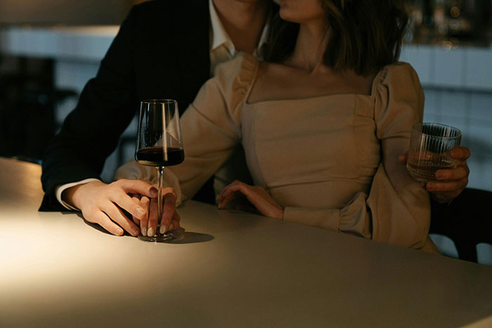 A couple at a bar, holding hands with glasses of wine, highlighting relationship challenges.