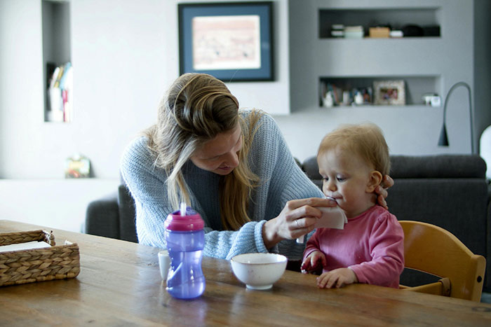 Nanny caring for a toddler at a dining table, showing nurturing interaction in a cozy home setting.