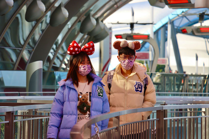 Two people wearing matching face masks and Disney-themed costumes walking on a futuristic path.