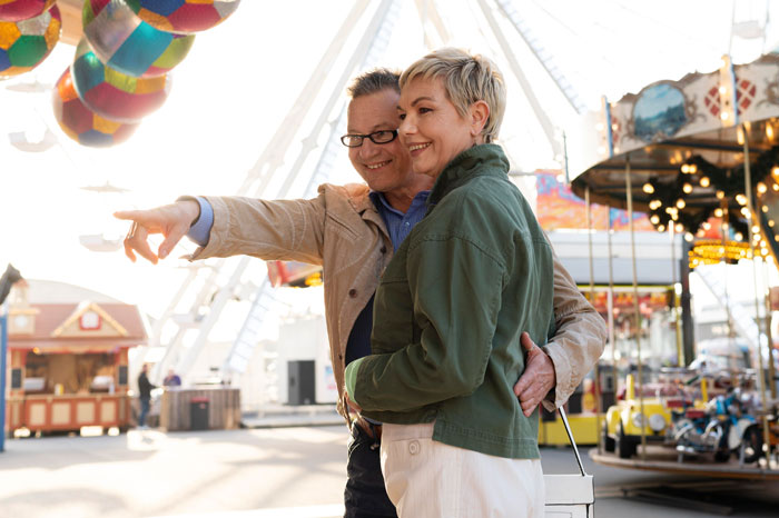 A couple enjoying a date at an amusement park, with colorful balloons and a Ferris wheel in the background.