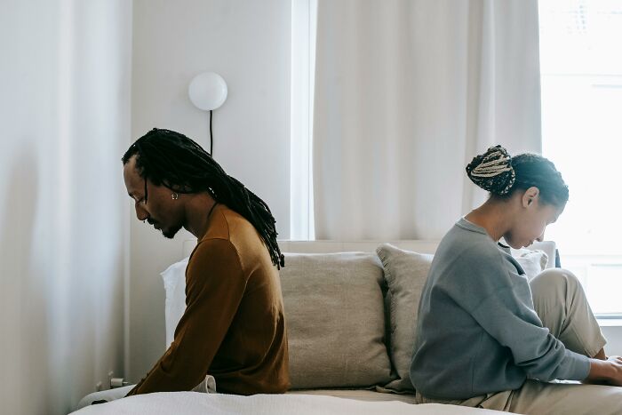 Couple sitting back-to-back on a bed, showing tension over commitment issues.