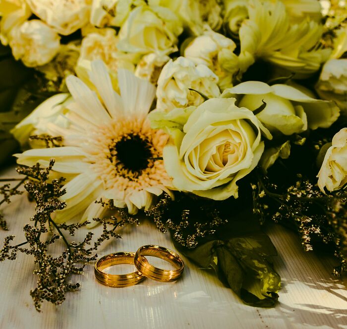 Wedding rings on a table with white roses, symbolizing commitment and marriage.