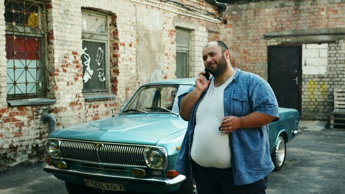 Man in casual attire stands by a vintage car, contemplating.