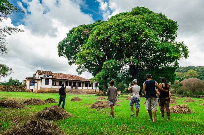 People walking towards a large country estate with a spacious lawn, indicating wealth.