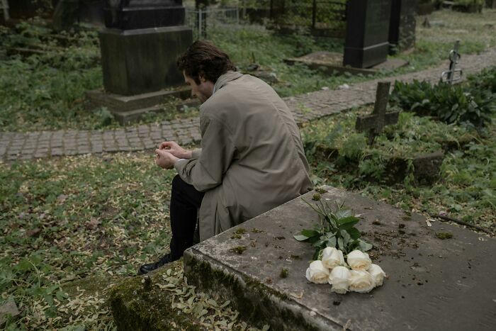 Person sitting by a grave with white roses, reflecting on how people unknowingly altered their bodies for the worse.