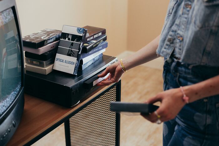 Person using a vintage VHS player and tapes, suggesting wealth from another era's luxury.