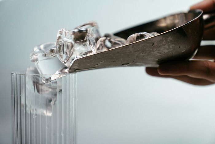 Silver scoop pouring ice cubes into a glass, showcasing luxury in a person's home.