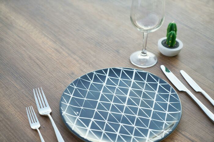 Geometric-patterned plate with utensils and a glass on a wooden table, beside a small cactus plant.