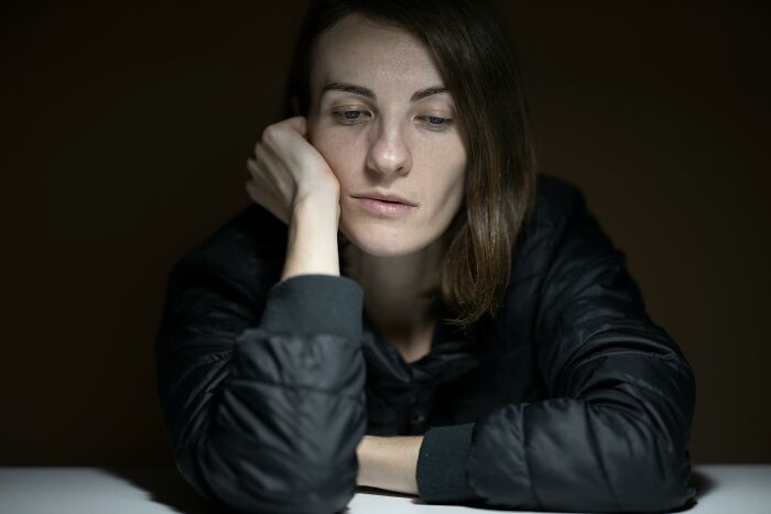 Person pondering, resting head on hand, wearing a dark jacket, in thoughtful reflection about body alterations.