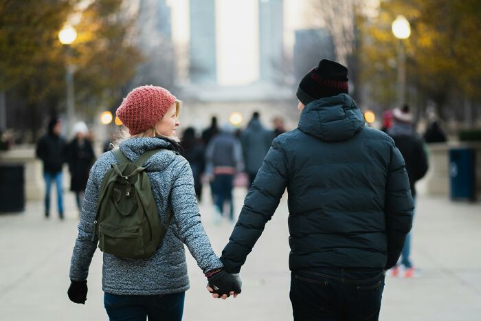 A couple walking hand in hand in a park, wearing winter clothes and backpacks, illustrating connection and introspection.