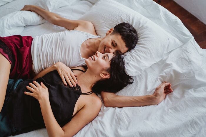 Couple lying in bed, smiling at each other, exploring effects of altering their bodies unknowingly.