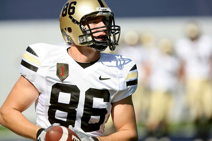 Football player in white jersey with number 86 holding a ball on the field, contemplating body changes.