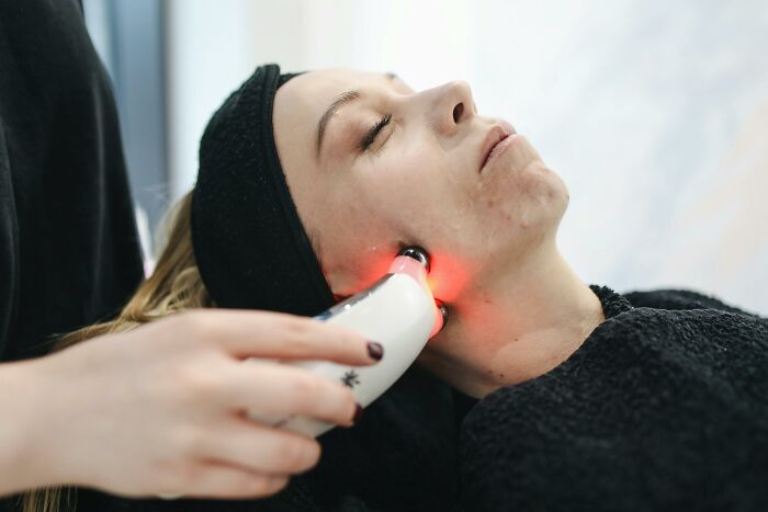 Person undergoing skin treatment with a device emitting red light, possibly altering body appearance.