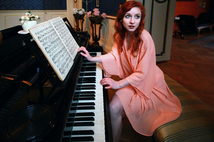 Woman in elegant dress sitting at grand piano, indicating wealth in someone's home.