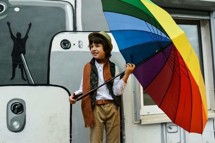 Child with a colorful umbrella stands by a mural, contemplating body alterations.