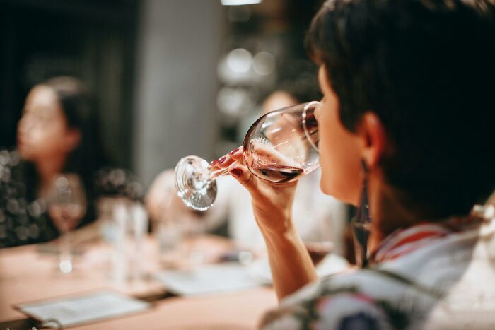 Person drinking wine at a social gathering, engaging in conversation, highlighting subtle body changes.