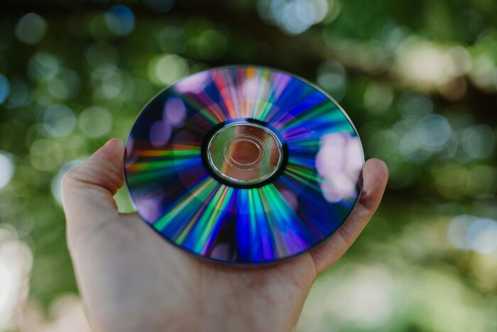 Hand holding a CD with reflective rainbow colors, symbolizing wealth and luxury in someone's home.