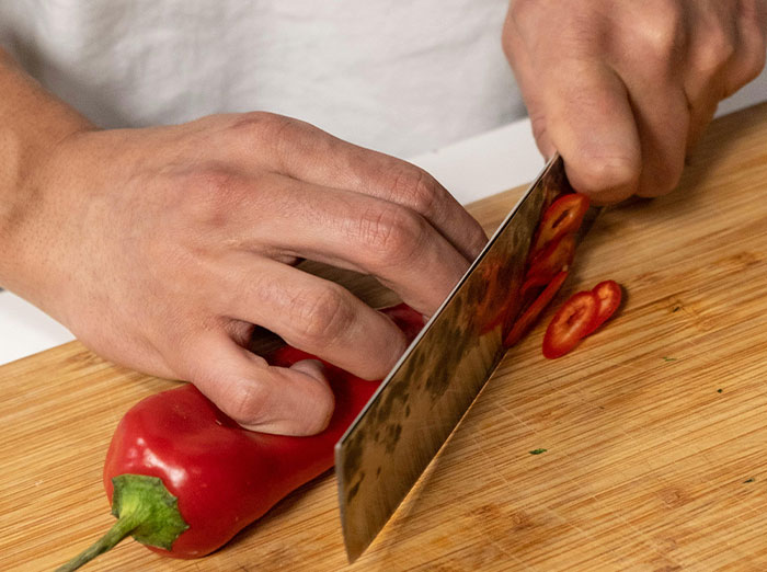 Person slicing red pepper on wooden board, setting a trap for food-thieving roommate.