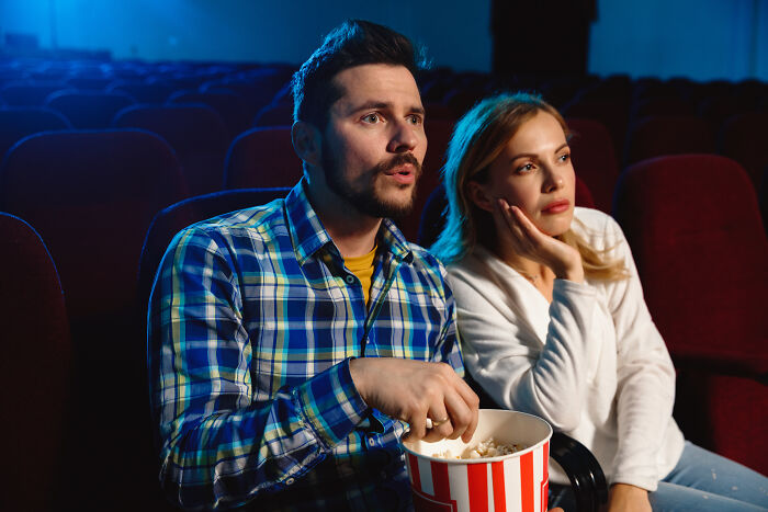 Couple in a movie theater, man holding popcorn, woman looking bored, related to moments not marrying someone.