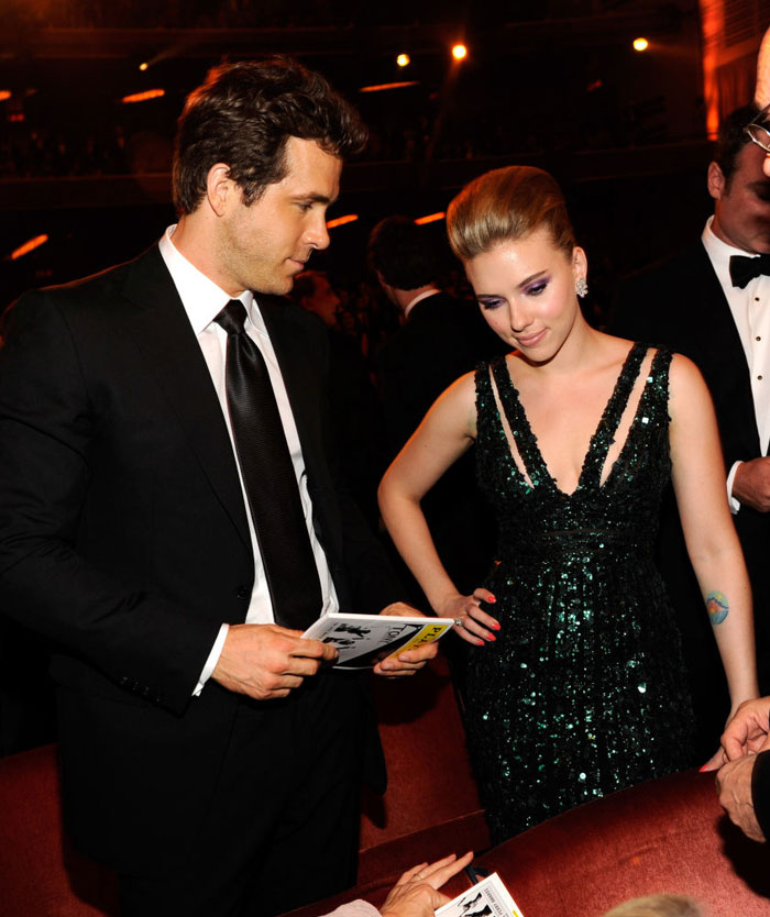 Scarlett Johansson in a sparkling green gown interacting at a formal event with Colin Jost, her husband, dressed in a black suit and tie.