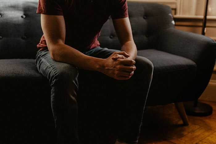 Person sitting on a couch with hands clasped, reflecting signs of a marriage destined to fail.