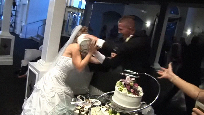 Bride and groom having a cake fight at a wedding reception, hinting at marriage difficulties.