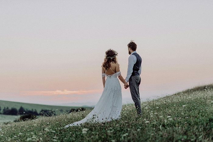 Couple in wedding attire holding hands in a field at sunset, representing signs a marriage is destined to fail.